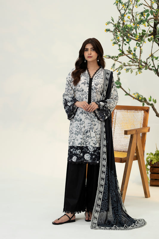 Woman wearing a black and white floral dress with a long black and white scarf, standing in a minimalistic setting.