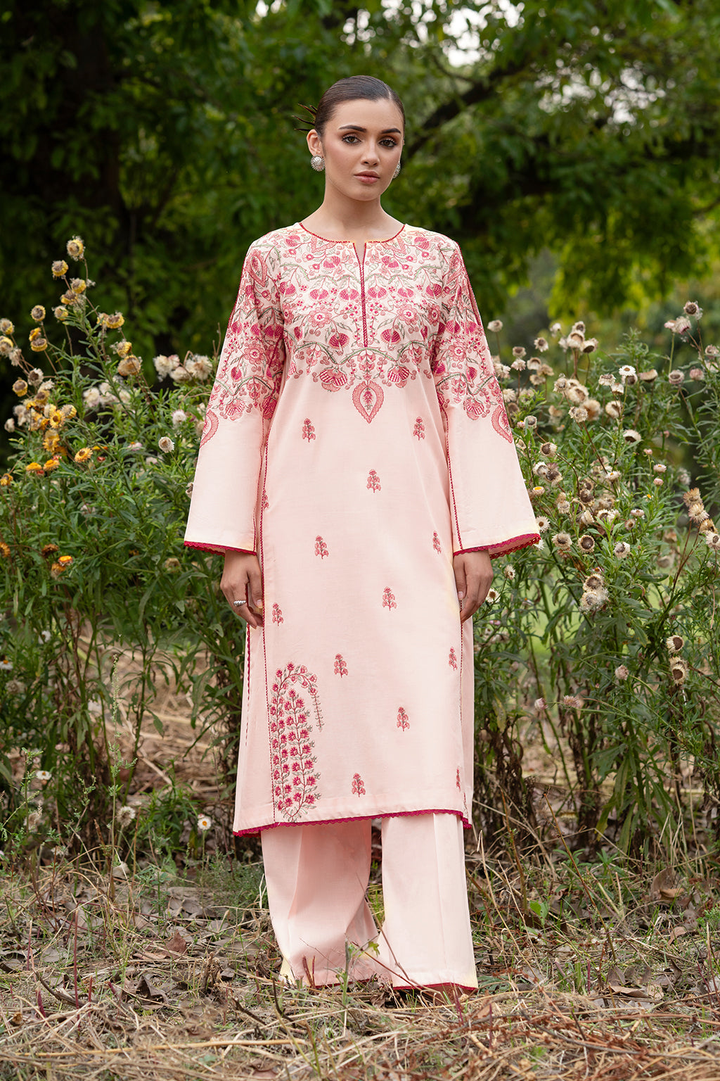 Woman in pink embroidered outfit standing in a floral setting