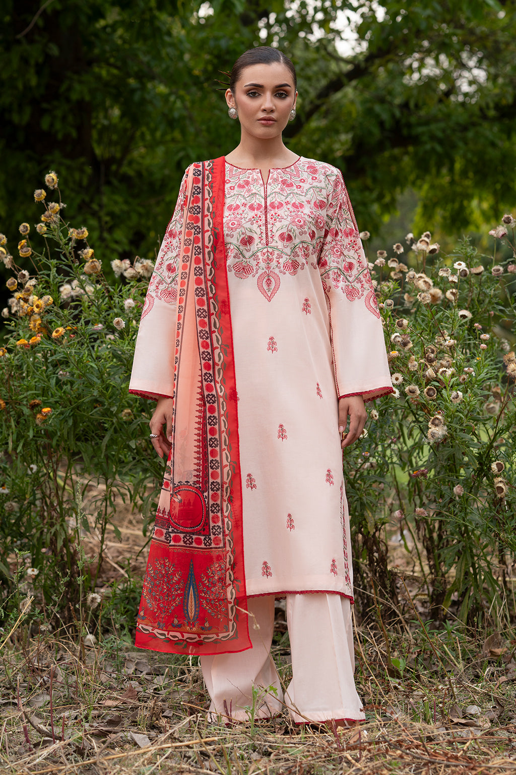A woman wearing a baby pink ensemble with vibrant multicolored embroidery, including a lawn embroidered front, sleeve panels, back, and a digital printed silk dupatta, paired with dyed lawn trousers.
