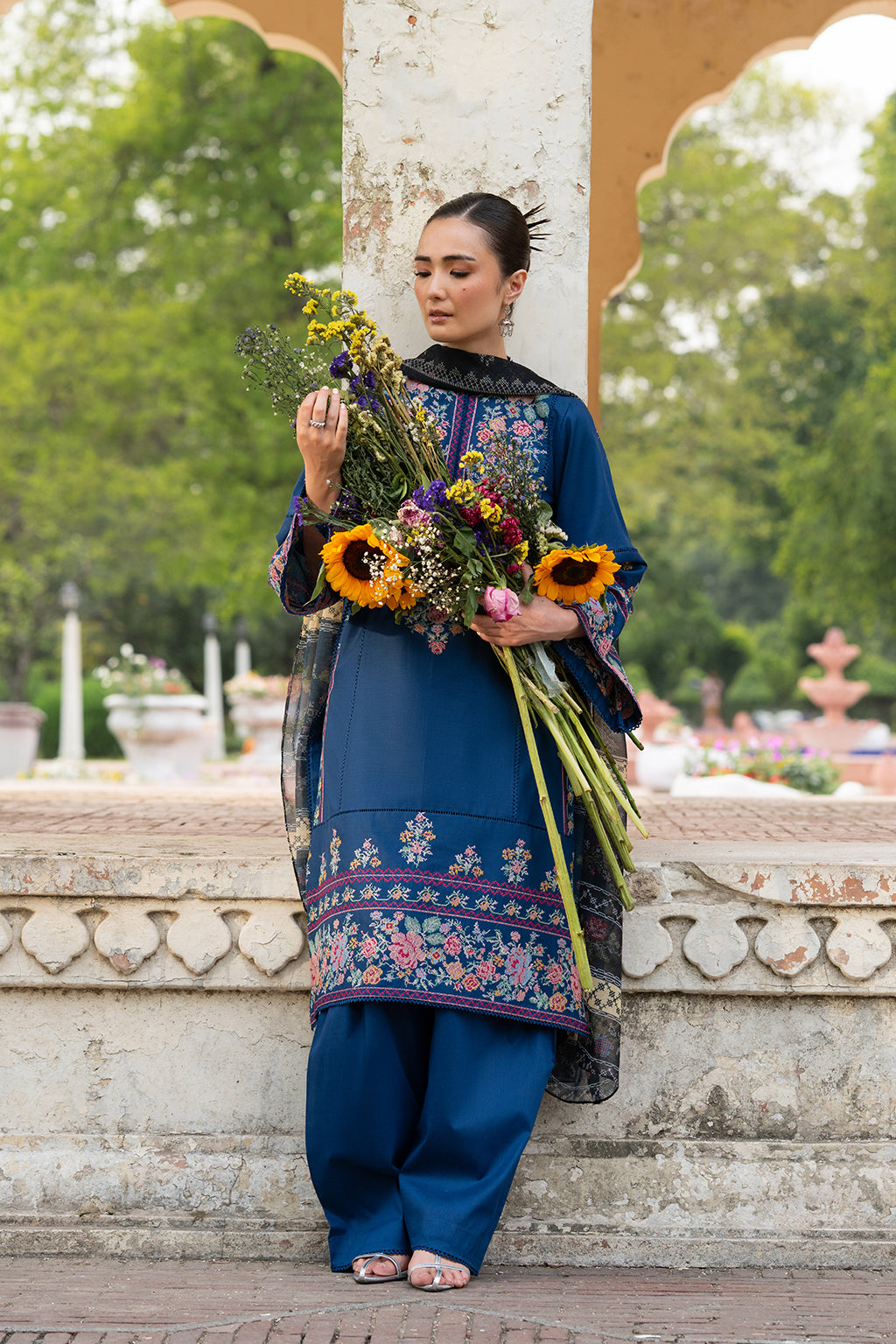 Woman in traditional outfit holding a bouquet of flowers outdoors