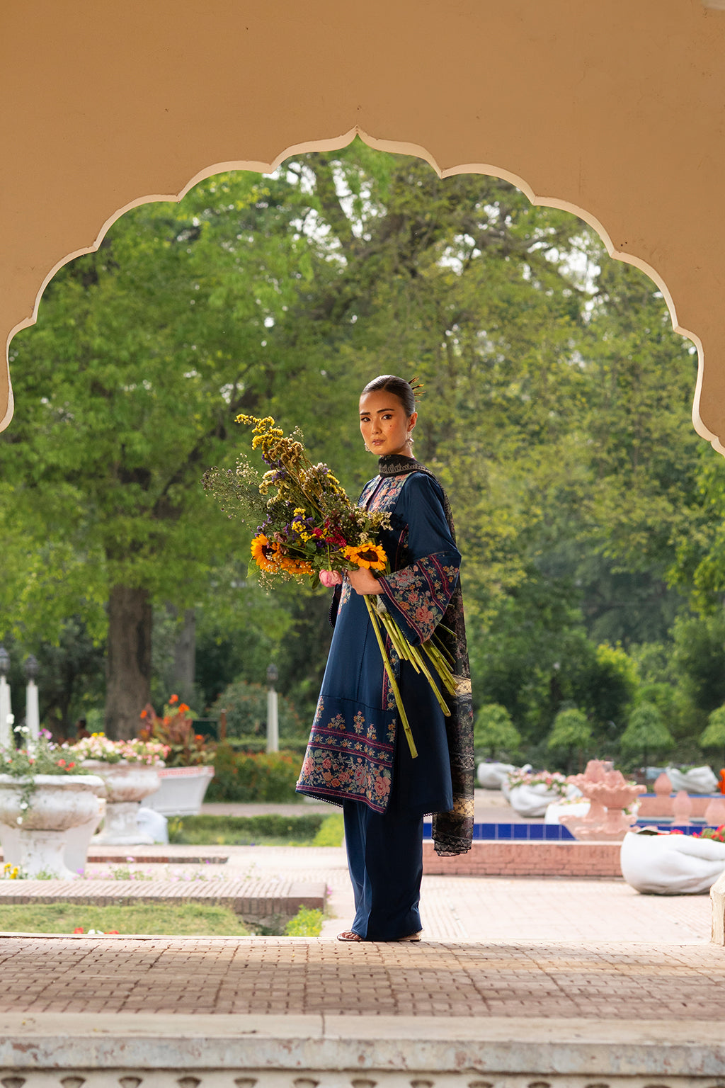 Person in traditional attire holding a bouquet in a garden setting.