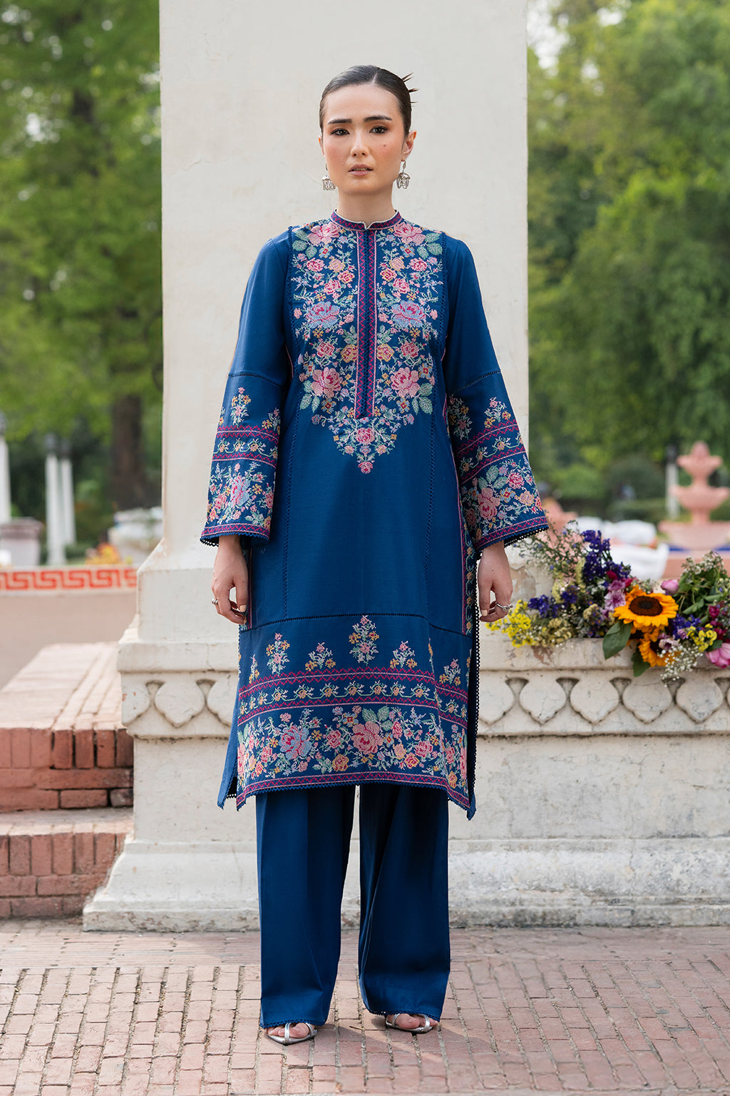 Person wearing a blue embroidered outfit in a garden setting.