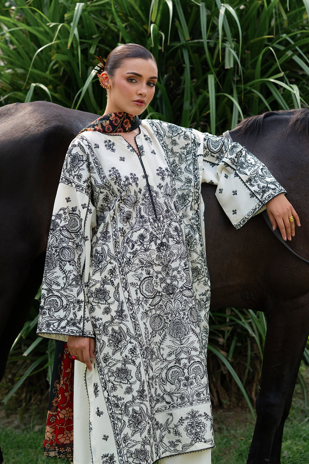 Woman in patterned outfit standing with a horse in a grassy area