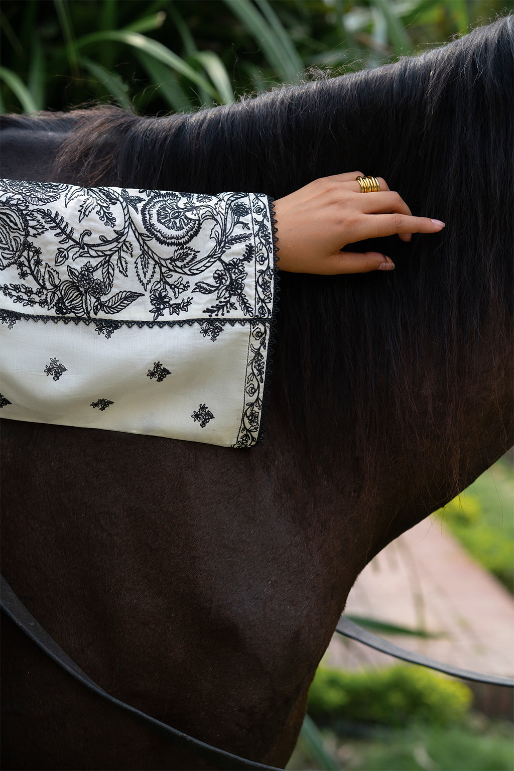 Person wearing a black and white embroidered sleeve touching a horse's neck.