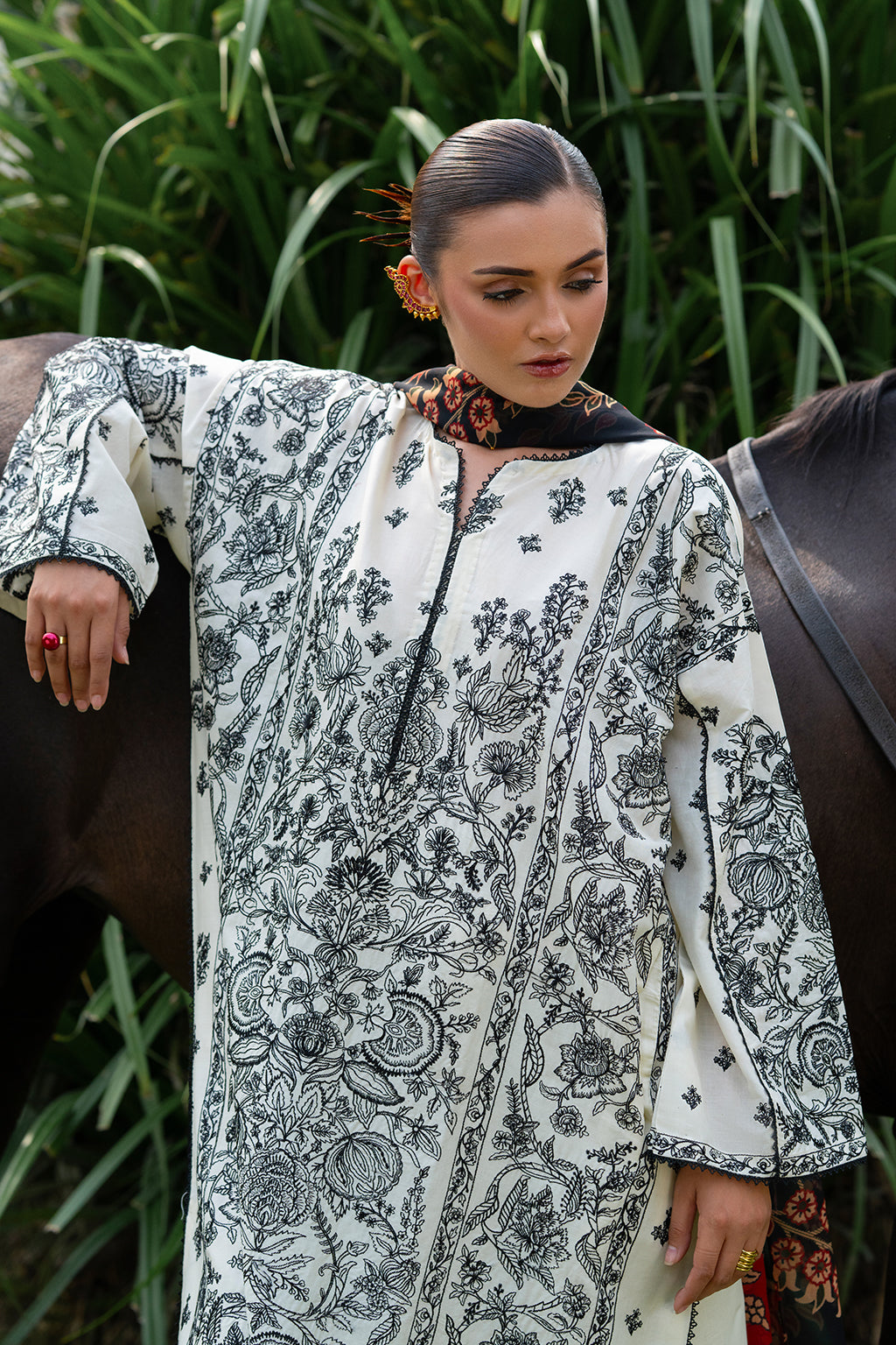 Woman in floral dress leaning on a horse with greenery in the background