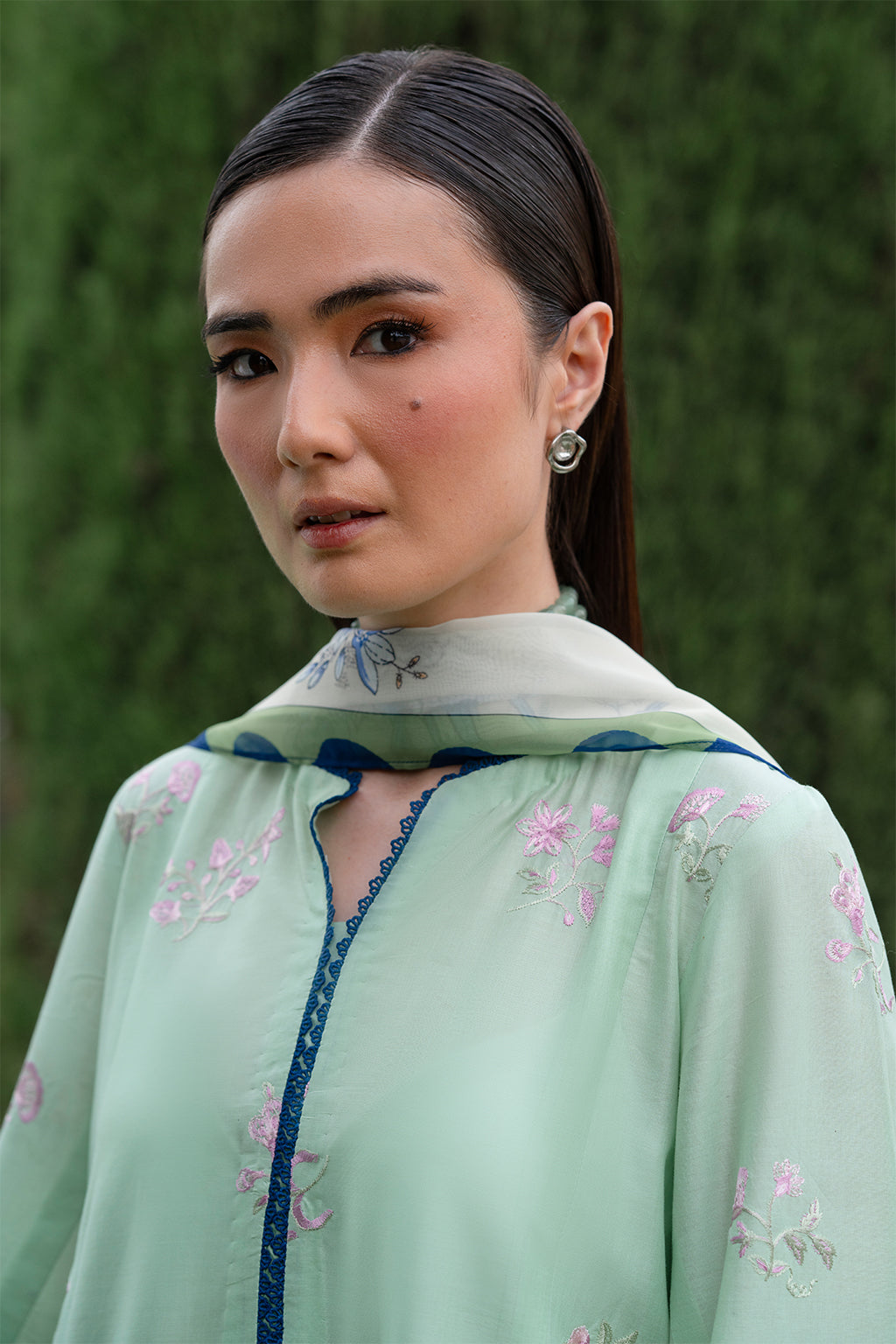 Woman in light green embroidered dress with blurred green background