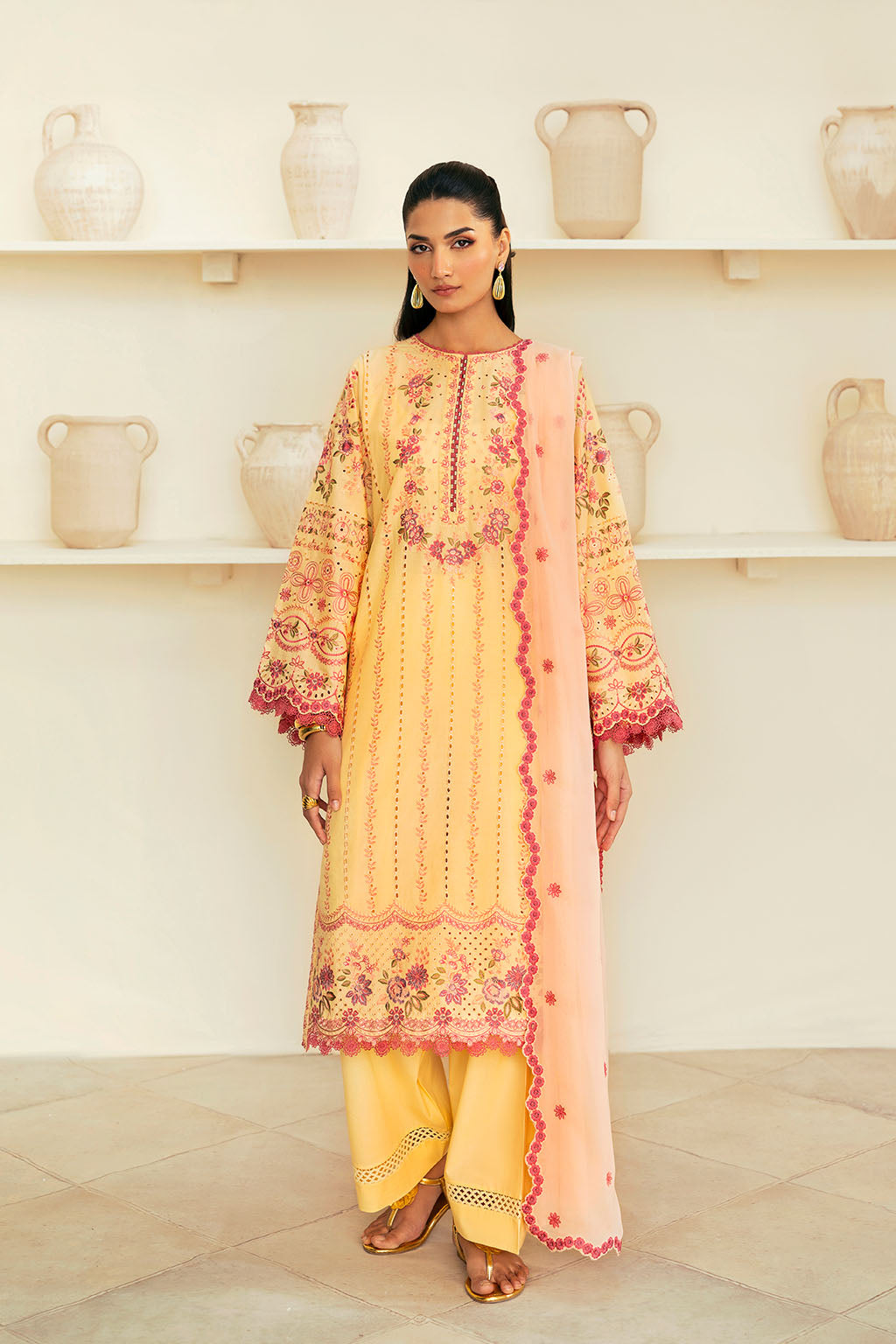 A woman wearing a traditional yellow dress with intricate embroidery and a chiffon dupatta.