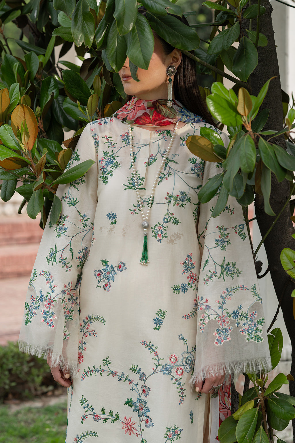 Person wearing a floral embroidered dress surrounded by greenery.