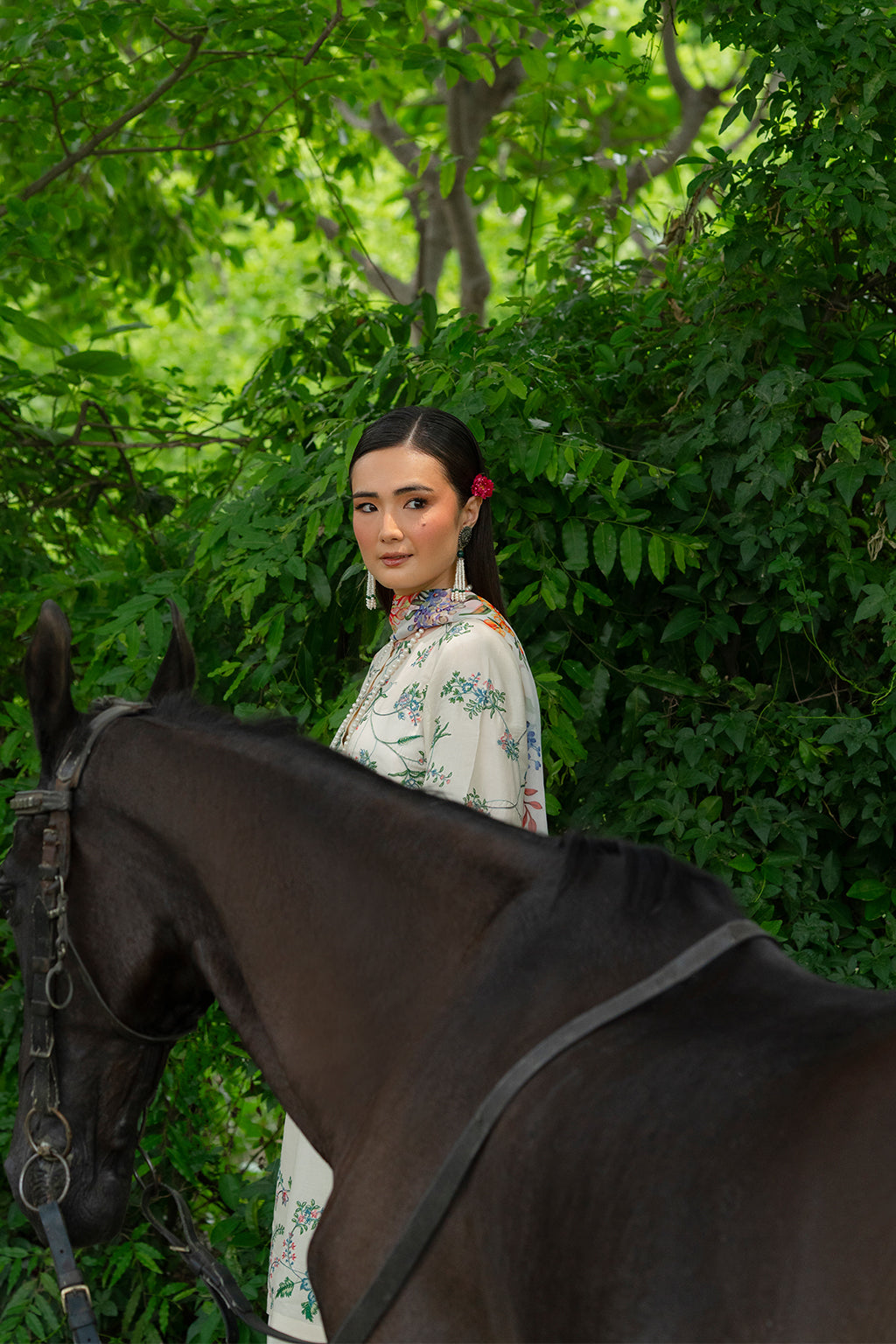 Woman in a floral dress sitting on a horse among greenery.