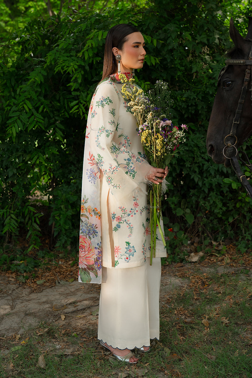 Woman in floral coat holding flowers standing by a horse.