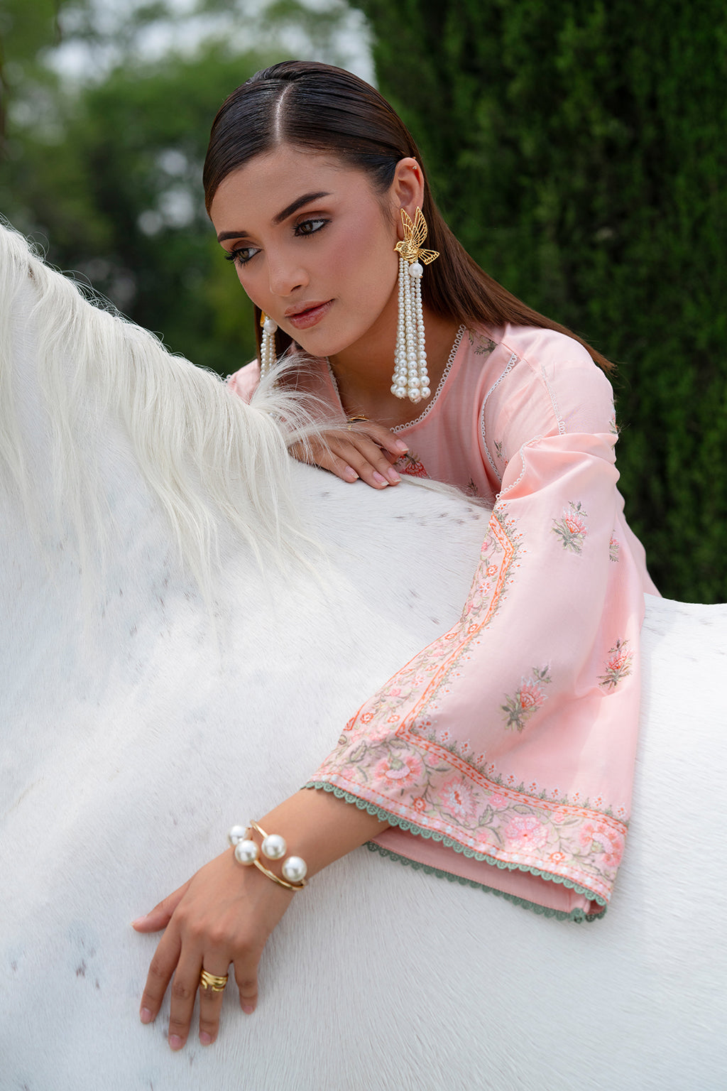 Woman in a pink traditional outfit sitting on a white horse.