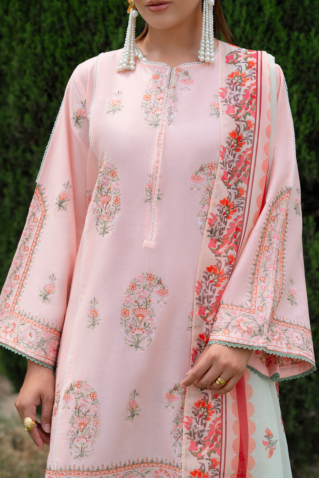 Light pink traditional dress with floral patterns against a green background.