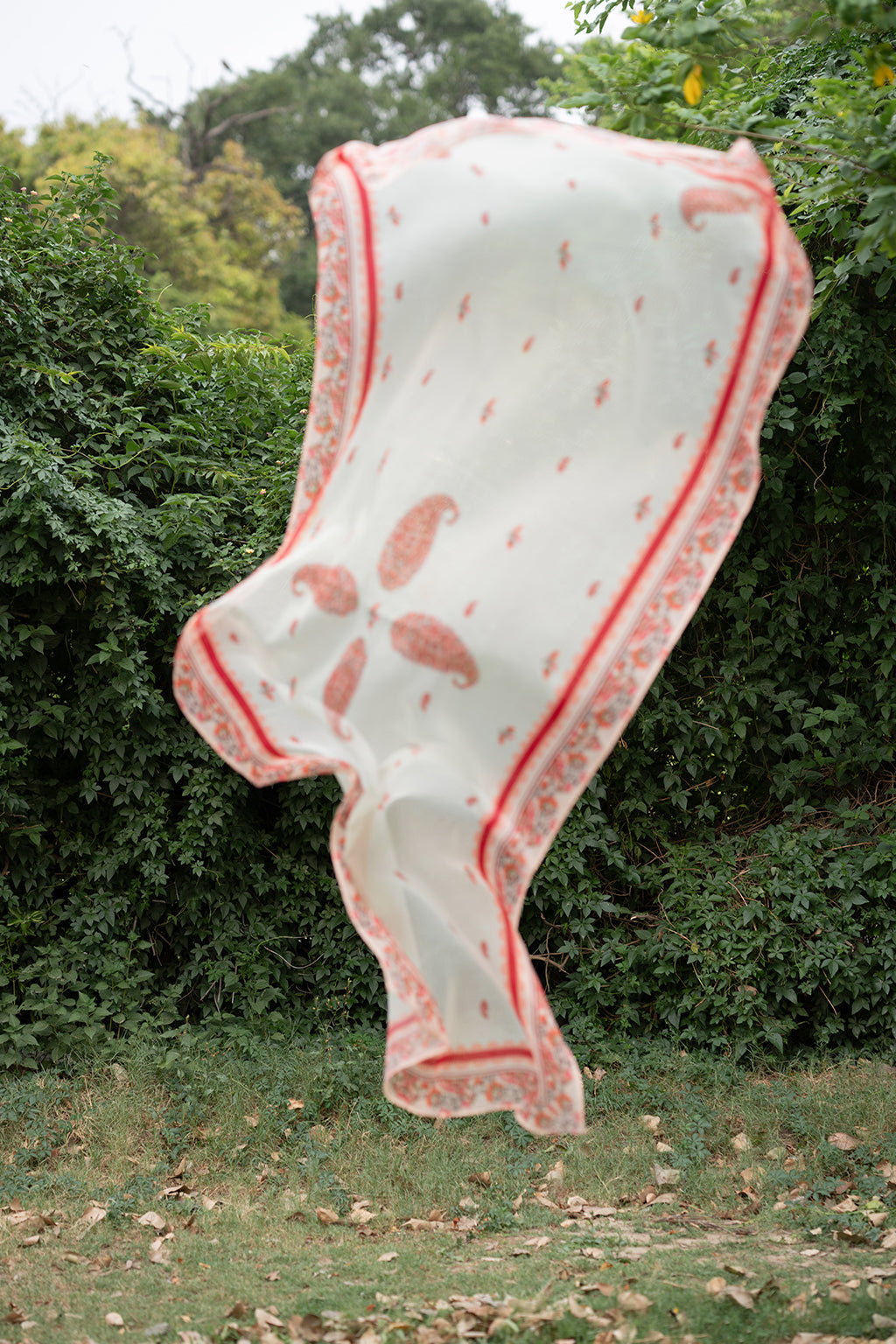 A woman joyfully holds a colorful dupatta by Deyar Official high in the air, showcasing its vibrant design