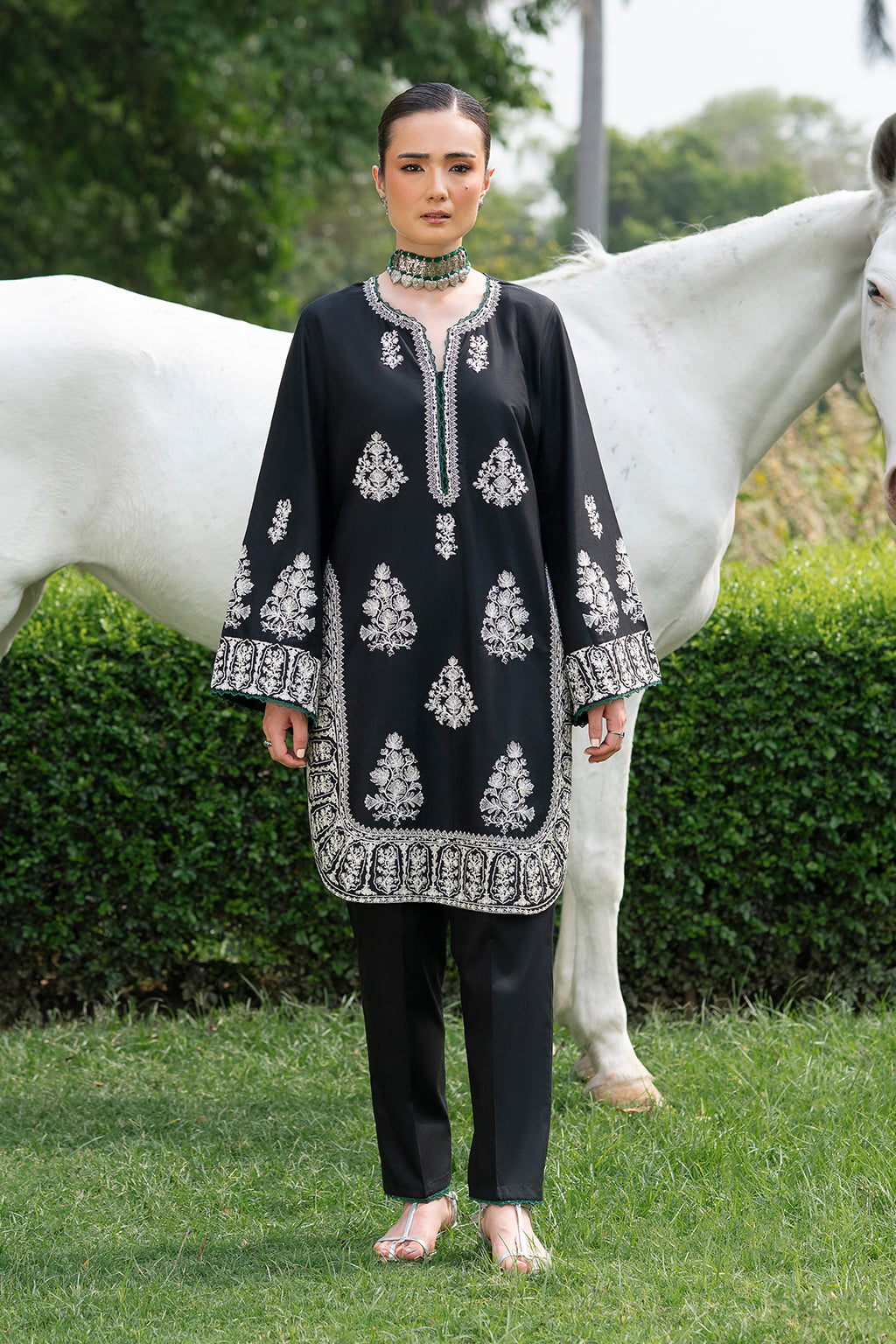 Person in black embroidered outfit standing in front of a white horse.