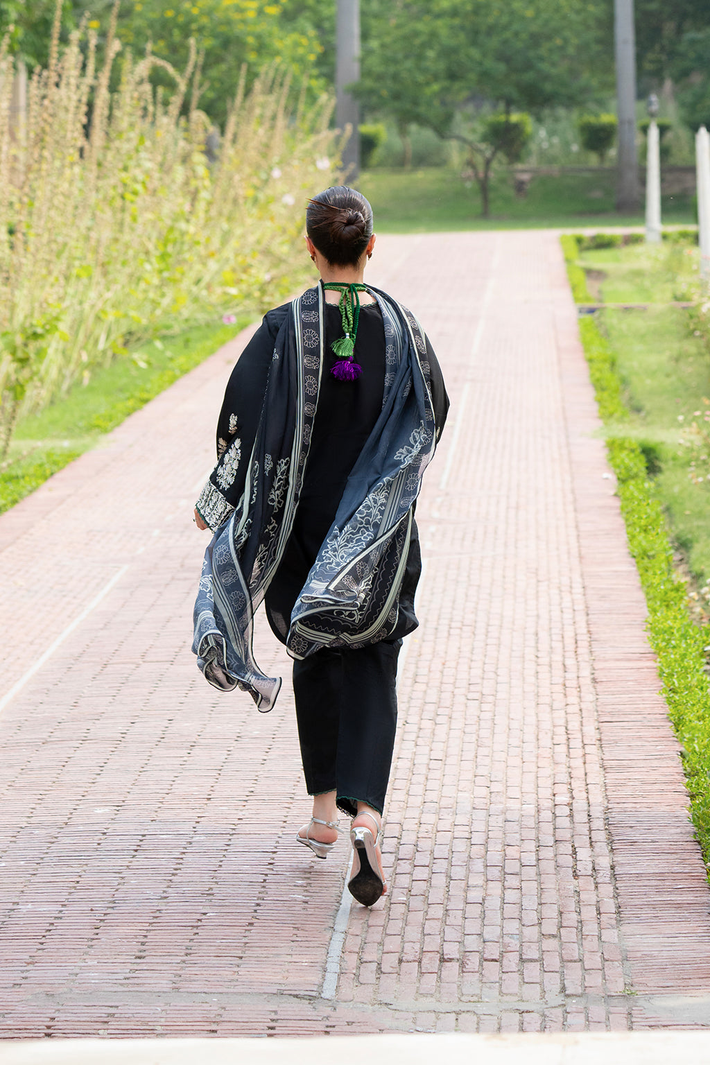 Person walking down a garden path wearing a patterned shawl.