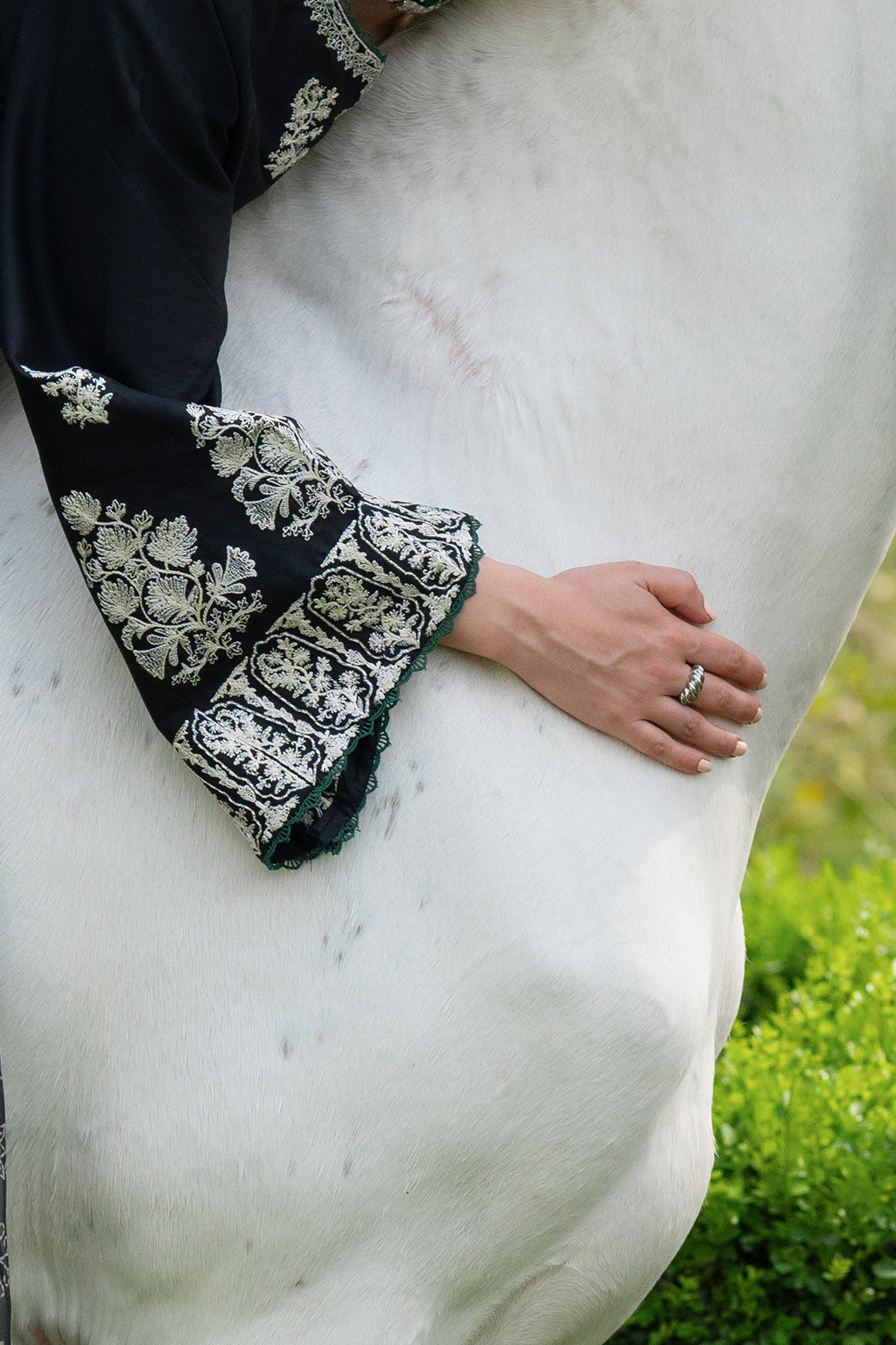 Person wearing a black garment with white floral patterns, holding a white horse.