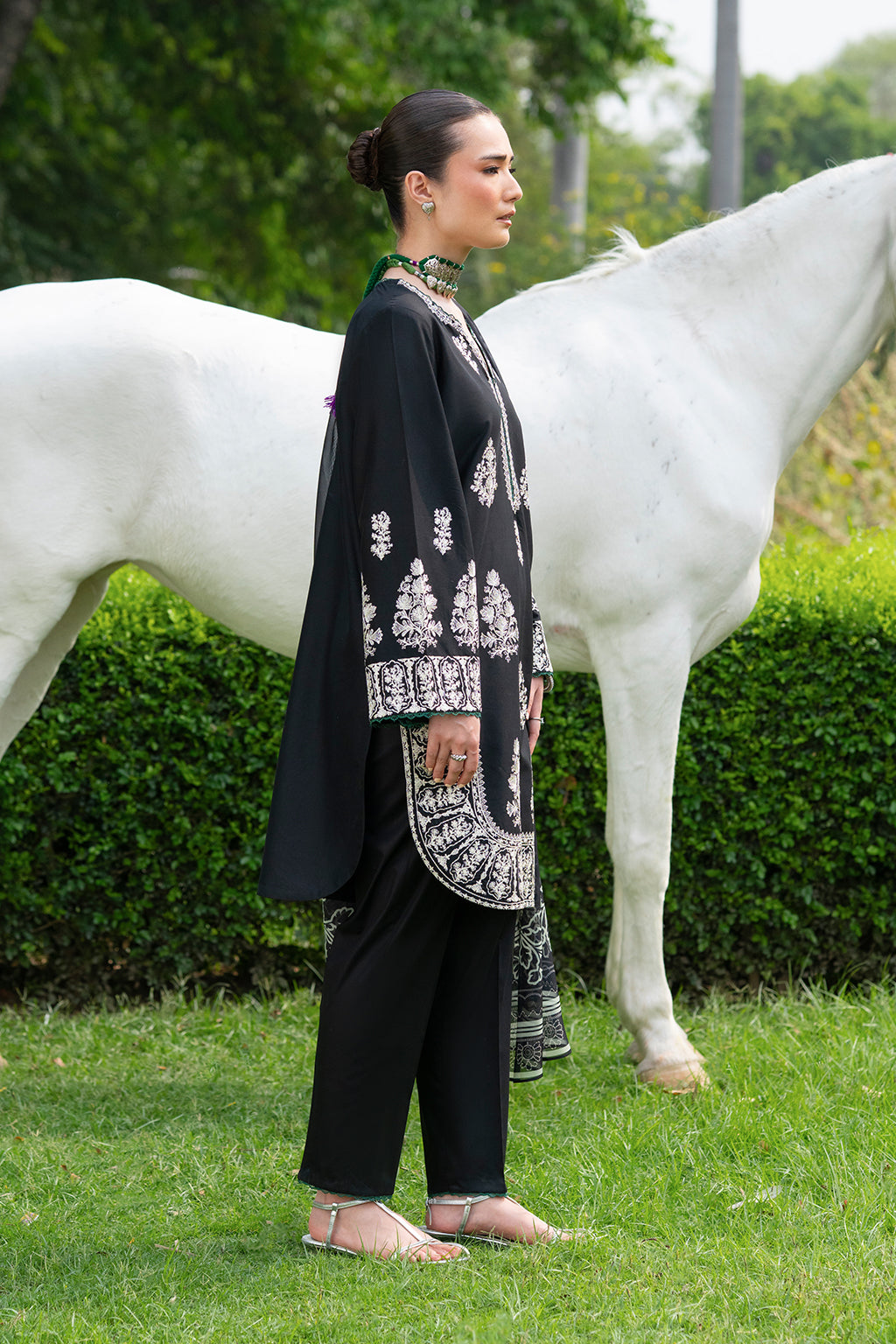 Woman in black outfit with white embroidery standing next to a white horse.