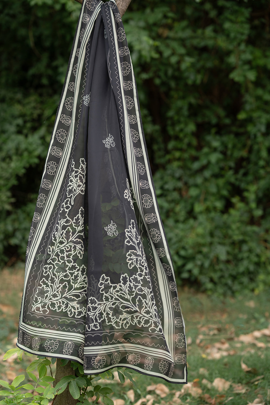 Black saree with white floral patterns hanging against a green background.