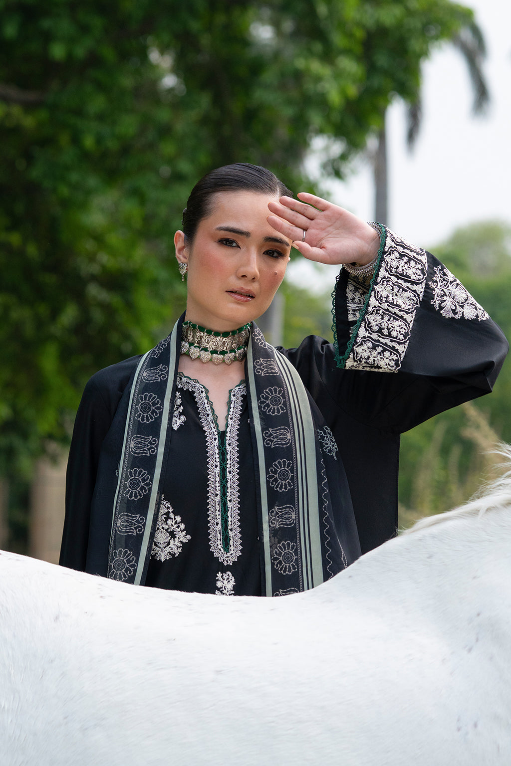 Person in traditional outfit with decorative elements, standing outdoors with trees in the background.