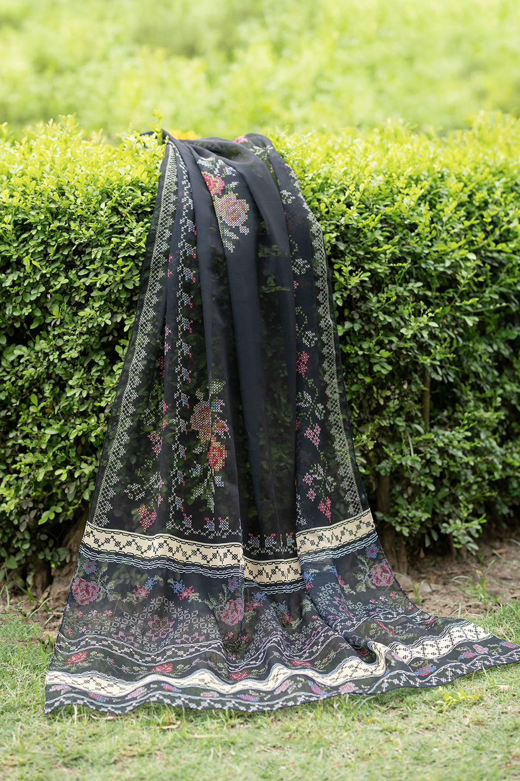 Black embroidered scarf on a hedge with grassy background
